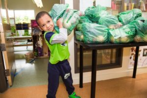A young boy lifts a prepackaged bag of produce off a table full of bags
