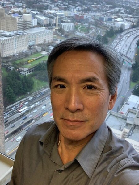 Selfie photo of Jeff Sakuma in front of his office window in Seattle Municipal tower