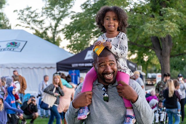 Black girl sitting on smiling Black man's shoulders at a community festival. Photo-1378866 by Brett Sayres on Pexels.com.