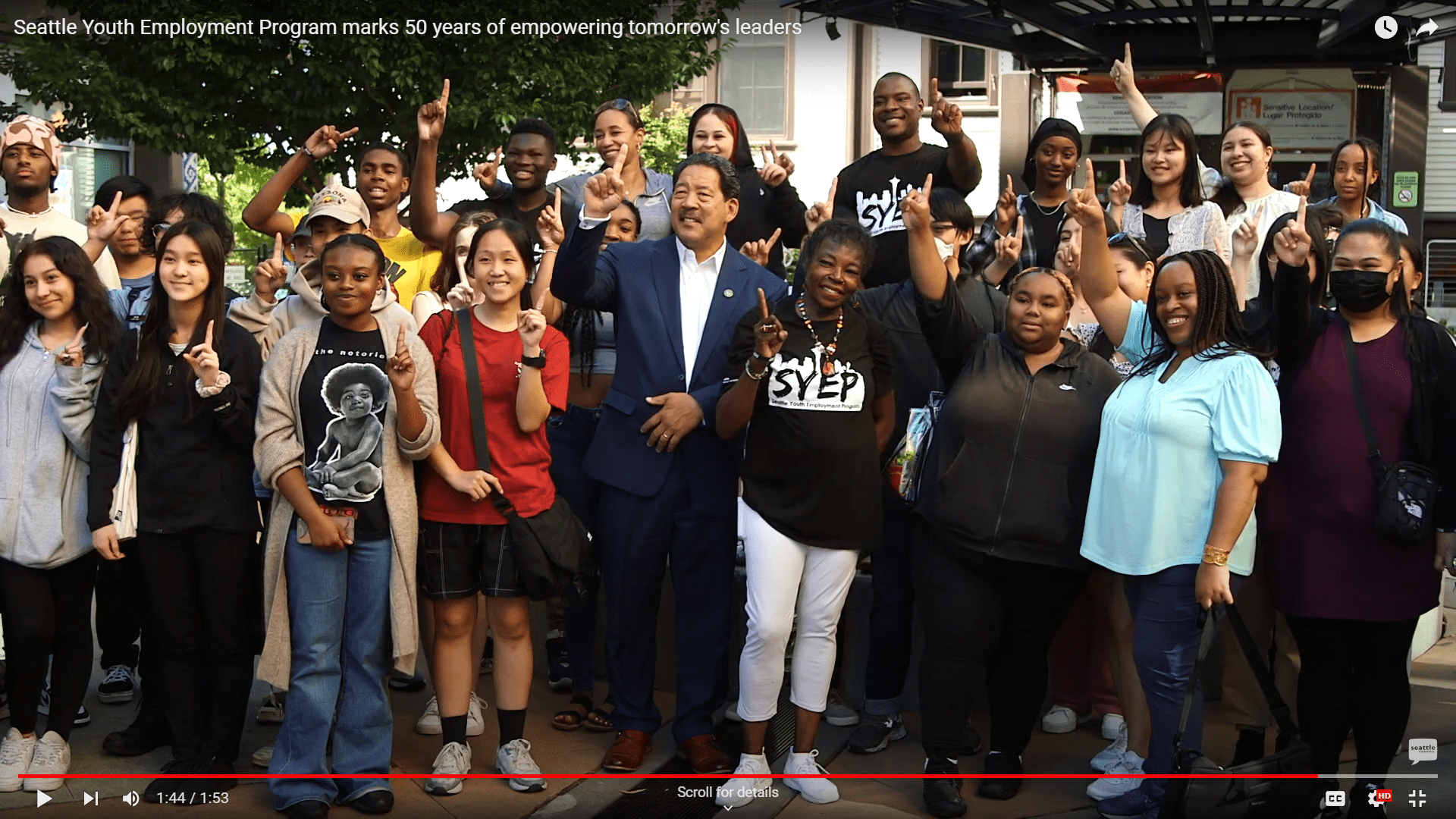 Screenshot of a Seattle Channel video on YouTube showing SYEP interns and staff posing for a group photo with Mayor Bruce Harrell with fingers raised in the air to signal #OneSeattle