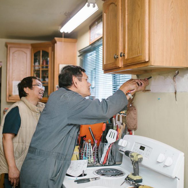 A technician from the Minor Home Repair program installs a kitchen range hood exhaust fan as a client looks on.