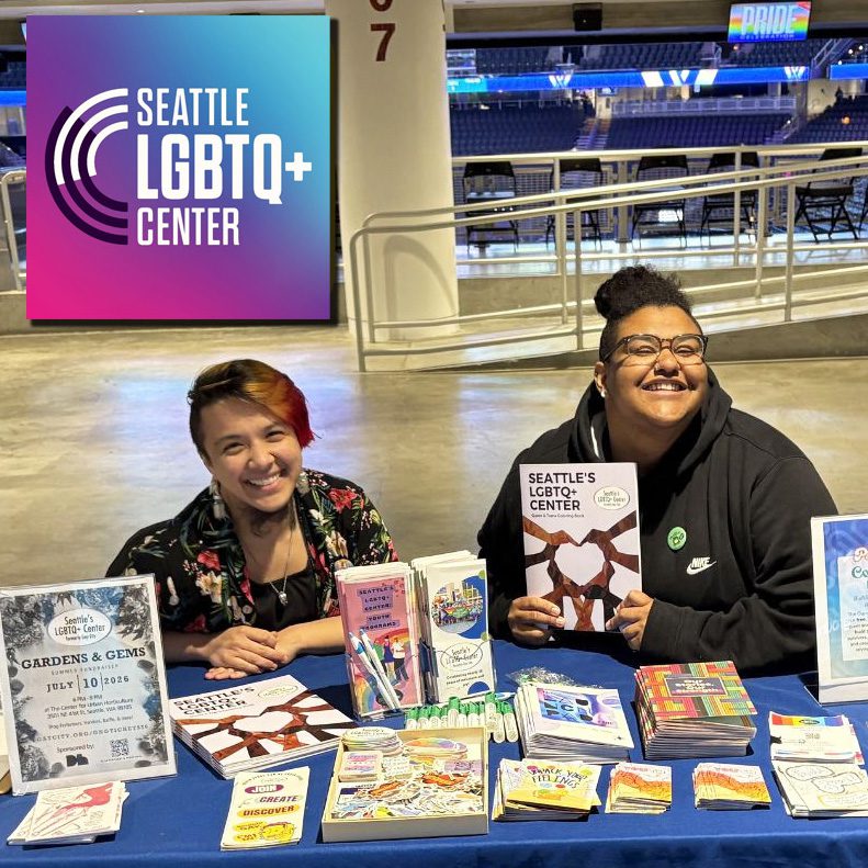 Two volunteers staff a table with literature for the Seattle LGBTQ+ Center.